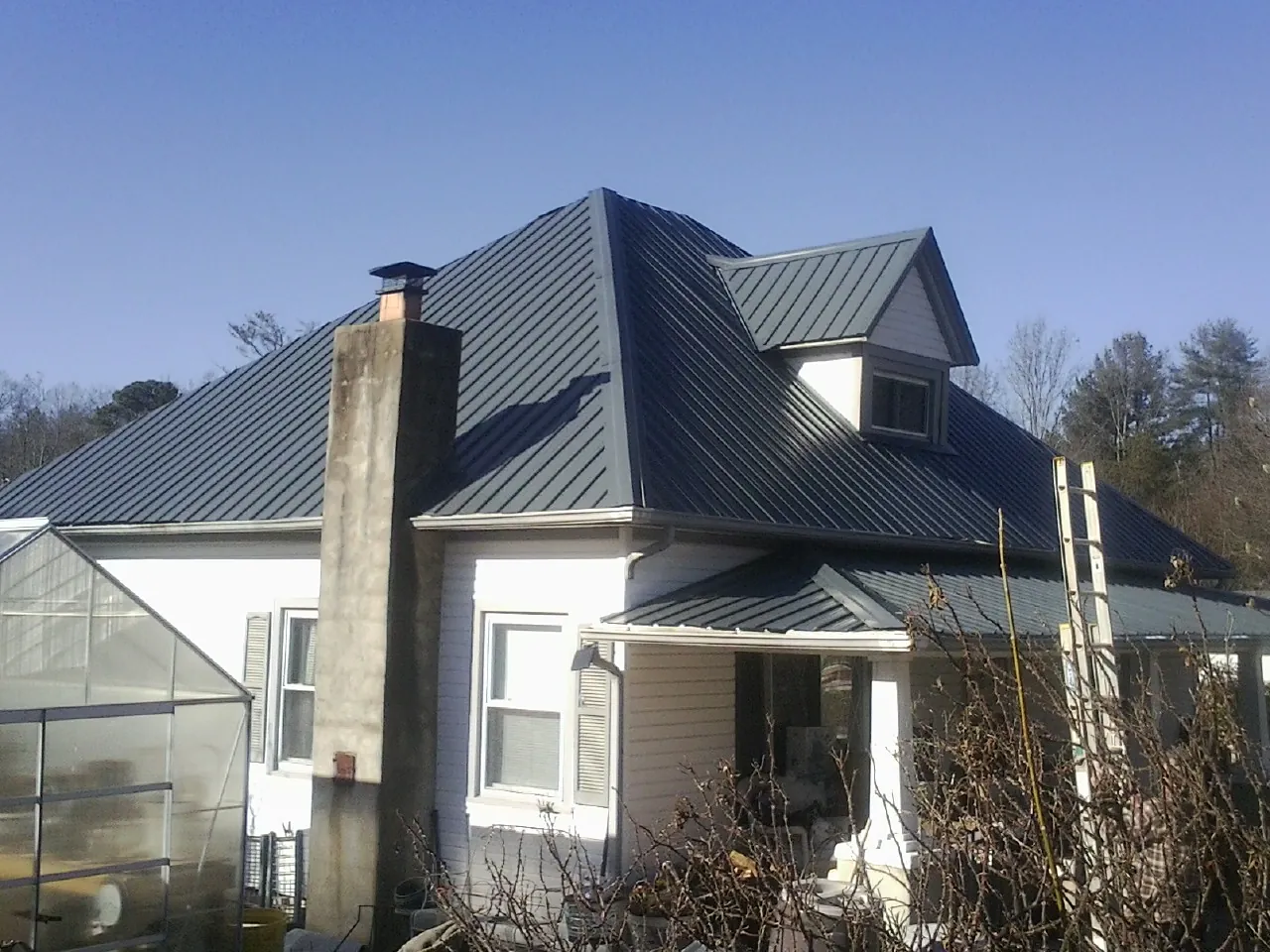 Dark blue standing seam metal roof on a white farmhouse with dormer — Slate & Tile Roof Repair by Roofing Brothers in Cohasset