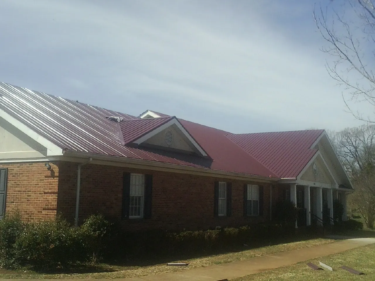 Red metal roof with gabled entries on a long brick building, from a Hail Damage Roof Repair job in Cohasset