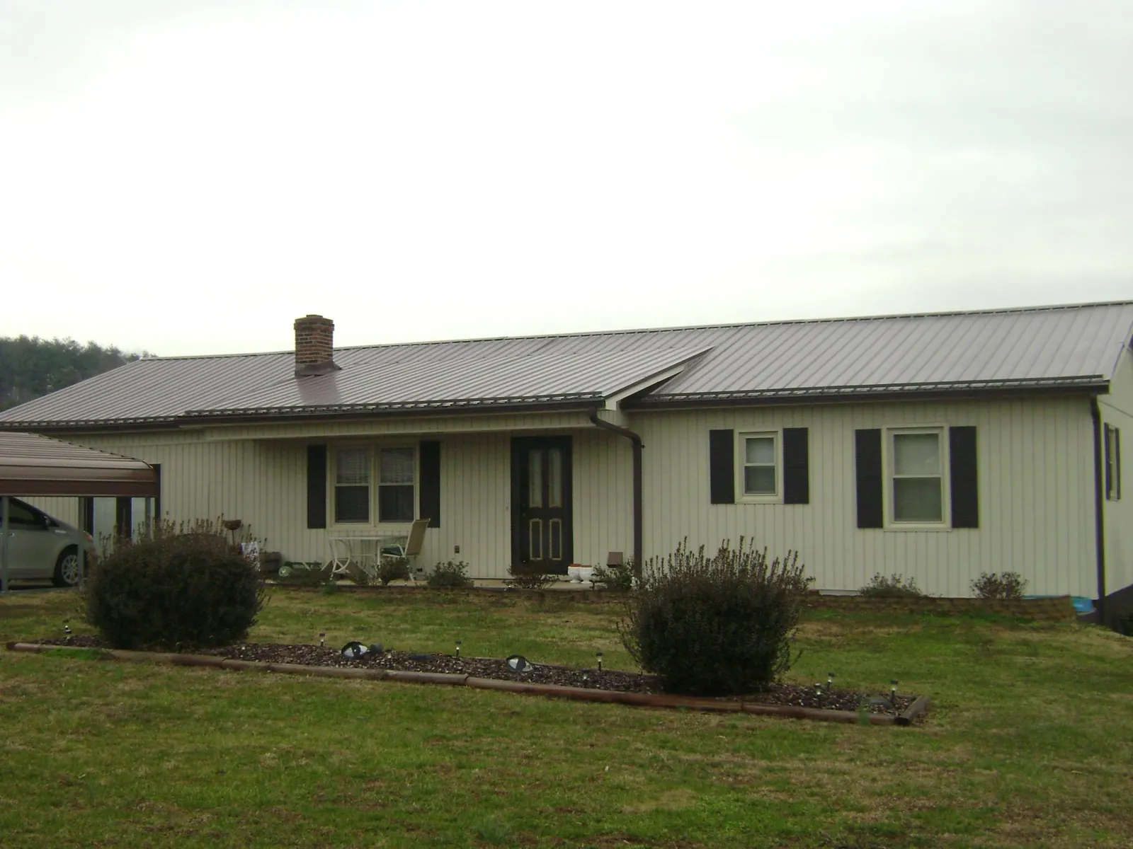 Brown metal roof on a cream sided ranch home with a brick chimney in Cohasset