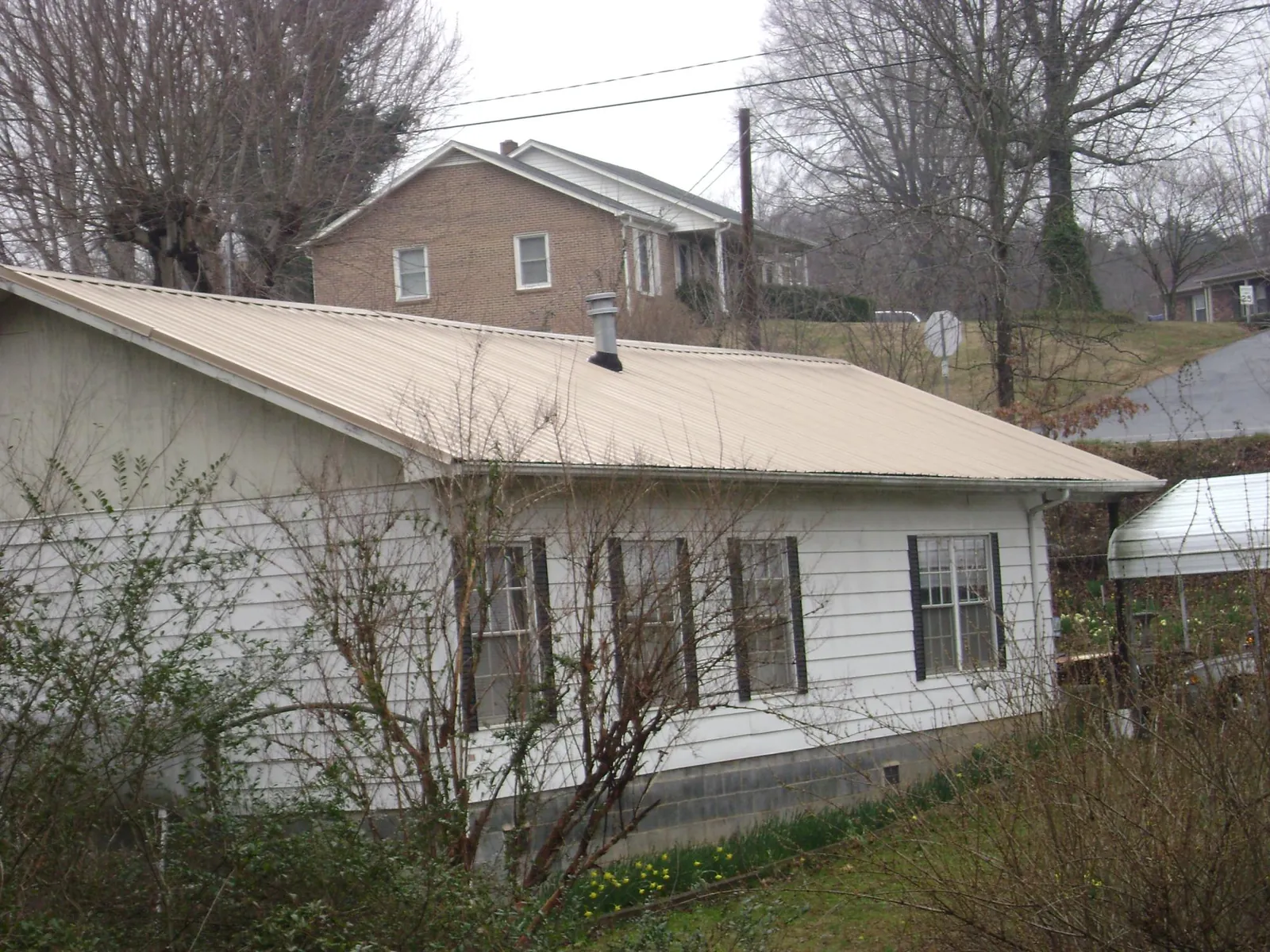 Tan metal roof on a white sided house set into a hillside — Commercial Roofing by Roofing Brothers in Cohasset