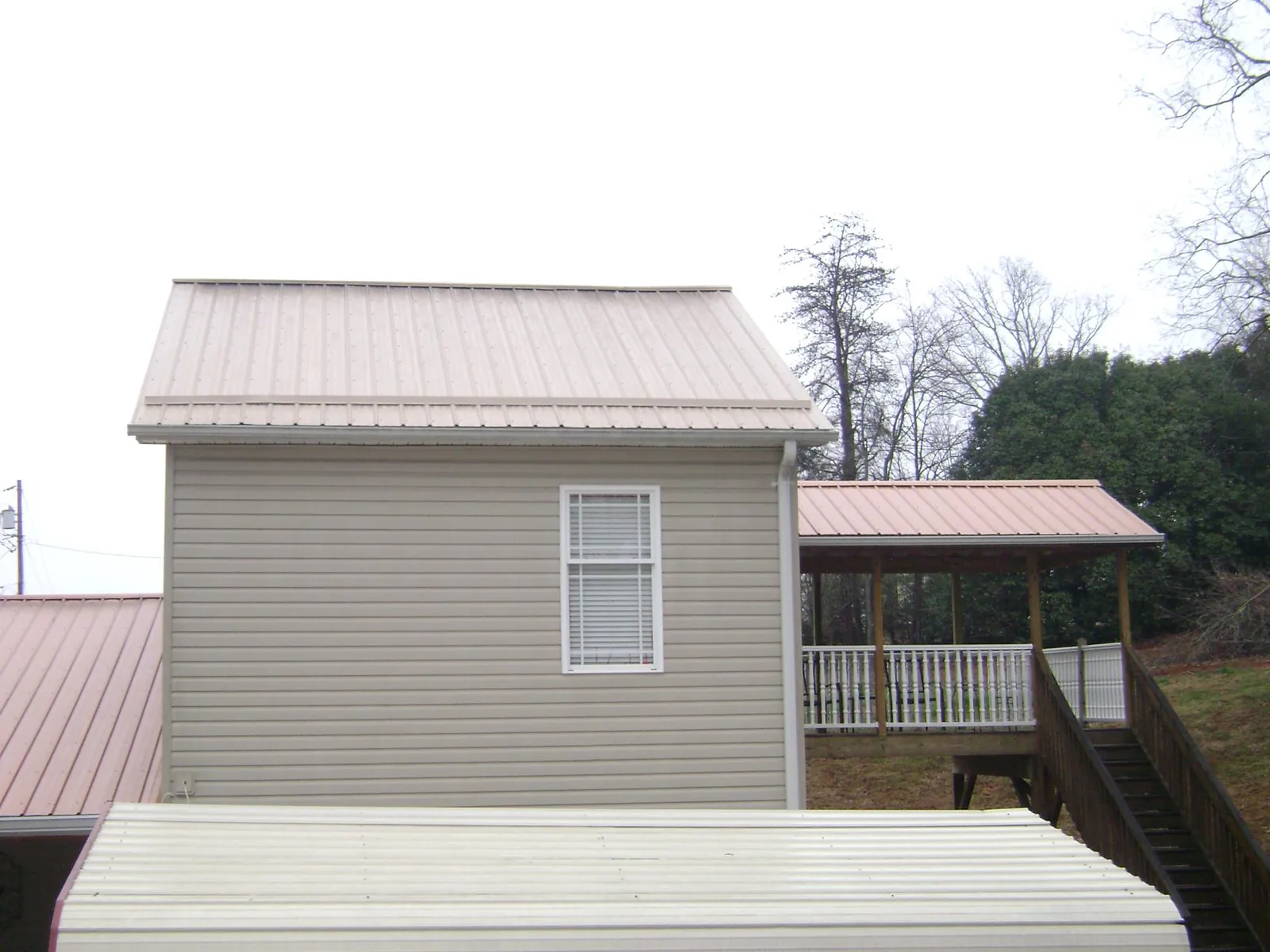 Tan metal roofs on a two story addition and attached porch, from a Roof Replacement job in Cohasset